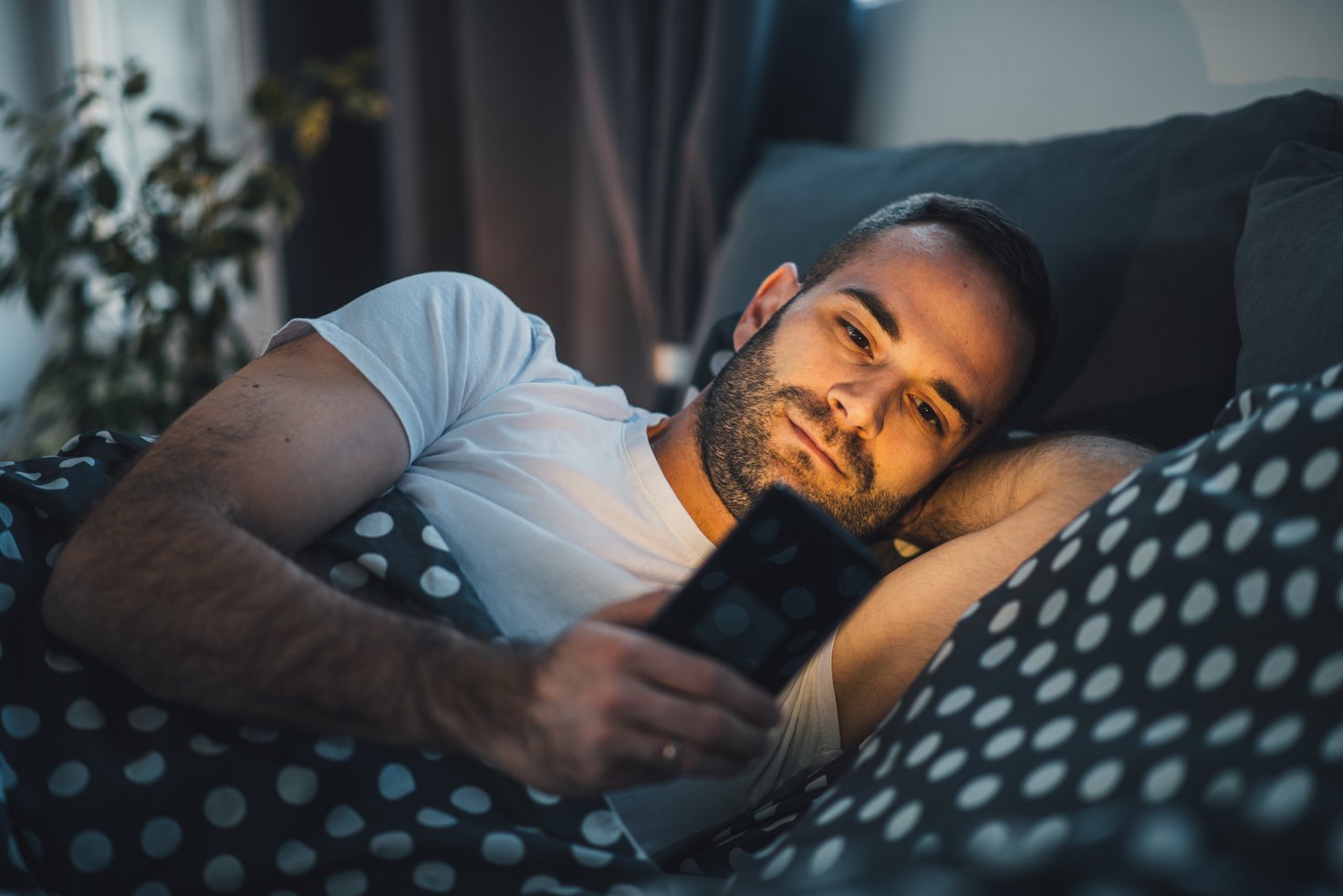 Young cell phone addict man in bed using smartphone